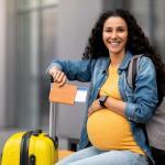 une femme enceinte est assise a côté de sa valise avec son passeport dans la main